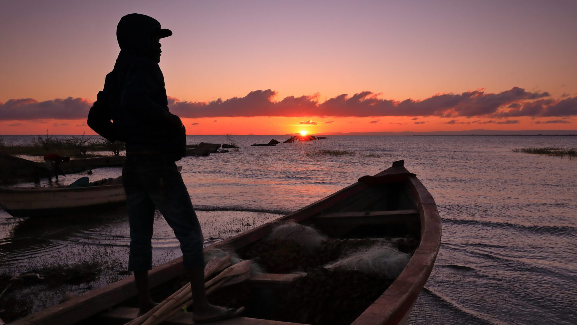 A man standing on the side of a boat in water.