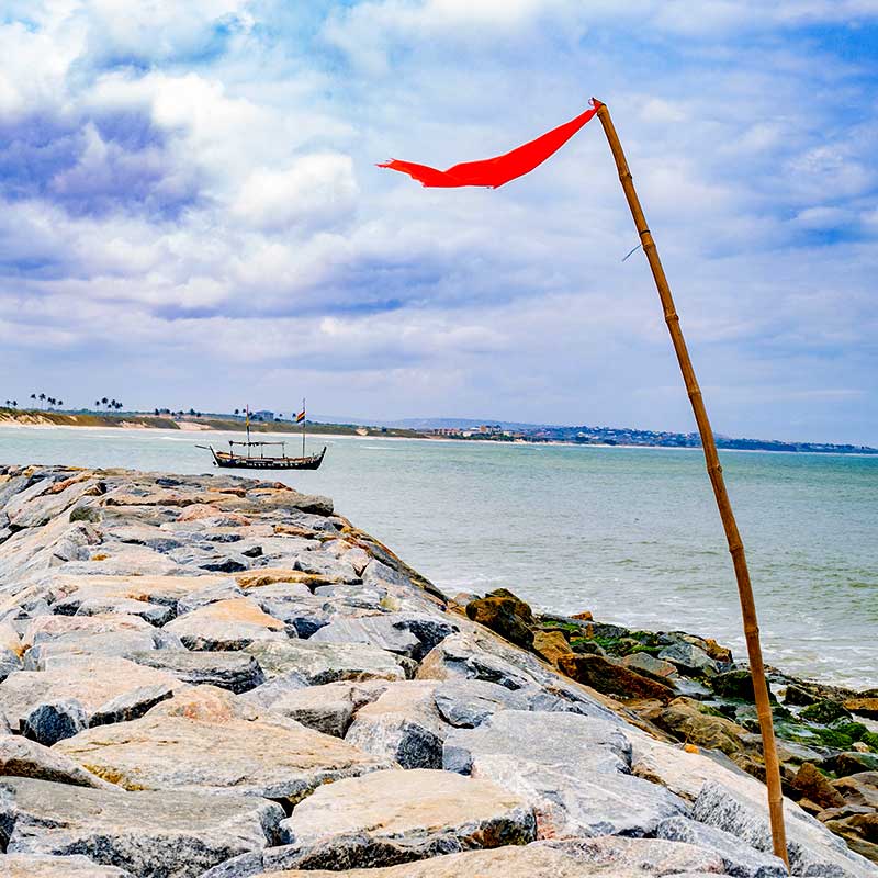 Stone pier stretching out into the ocean with a small red flag on it.