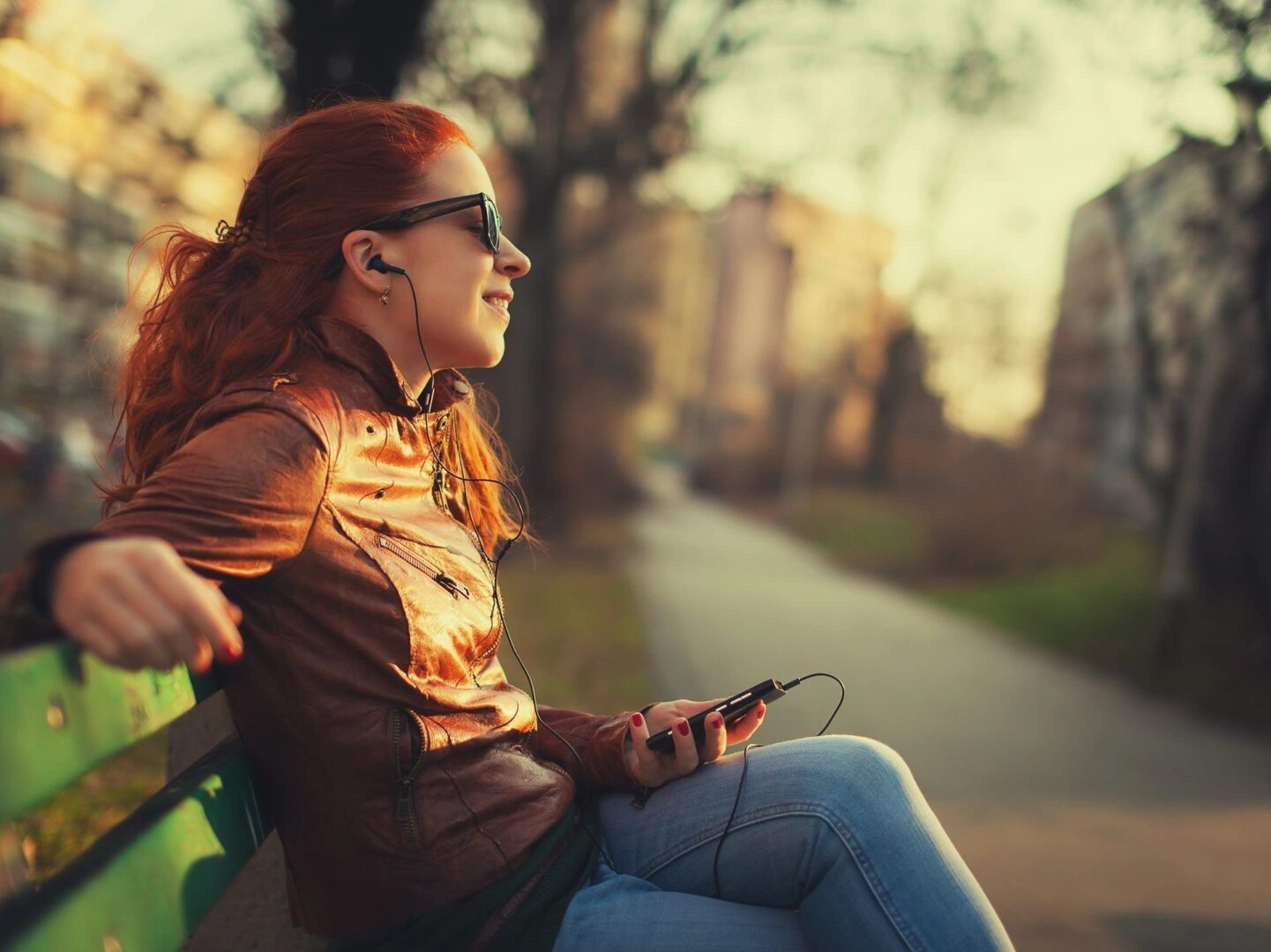 Woman listening to music from phone while sitting on park bench.